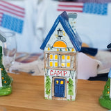 Decorative house-shaped lantern with 'CAMP' on a table, blurred background