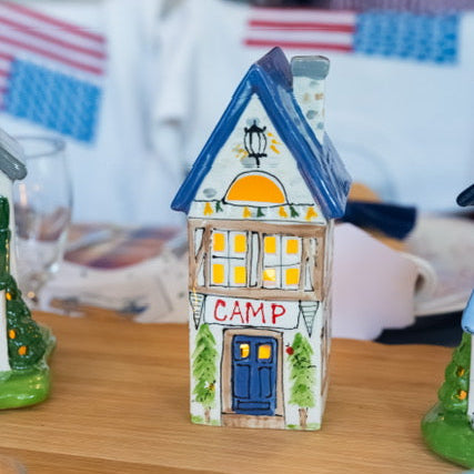 Decorative house-shaped lantern with 'CAMP' on a table, blurred background