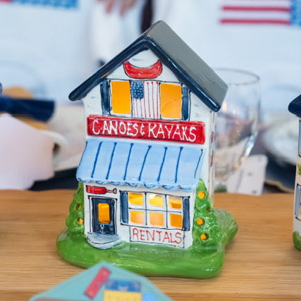 Colorful ceramic house-shaped ornament with 'Canoe & Kayak Rentals' text on a wooden surface.