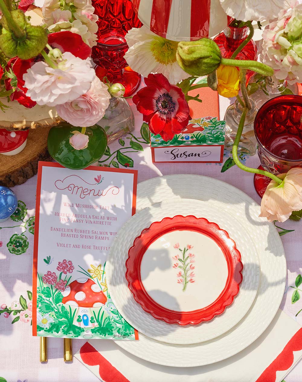Decorative table setting with red and white plates, floral centerpieces, and colorful place cards.