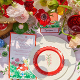 Decorative table setting with red and white plates, floral centerpieces, and colorful place cards.